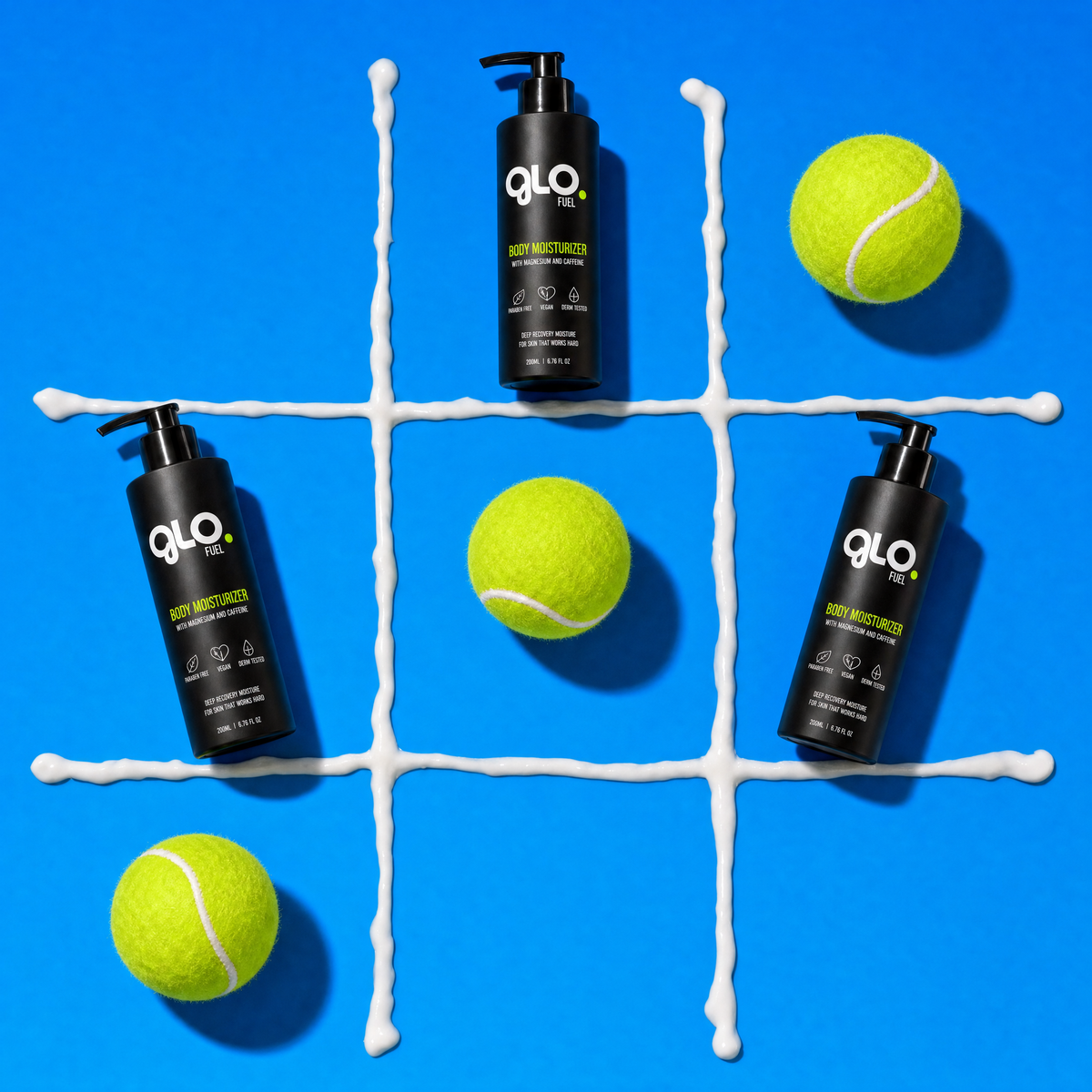 Three black pump bottles of QLO+ Anti-Muscle Pain Relief Cream are arranged on a bright blue background with a white tic-tac grid and four yellow tennis balls. The GLOFUEL brand name is clearly visible on the bottles.