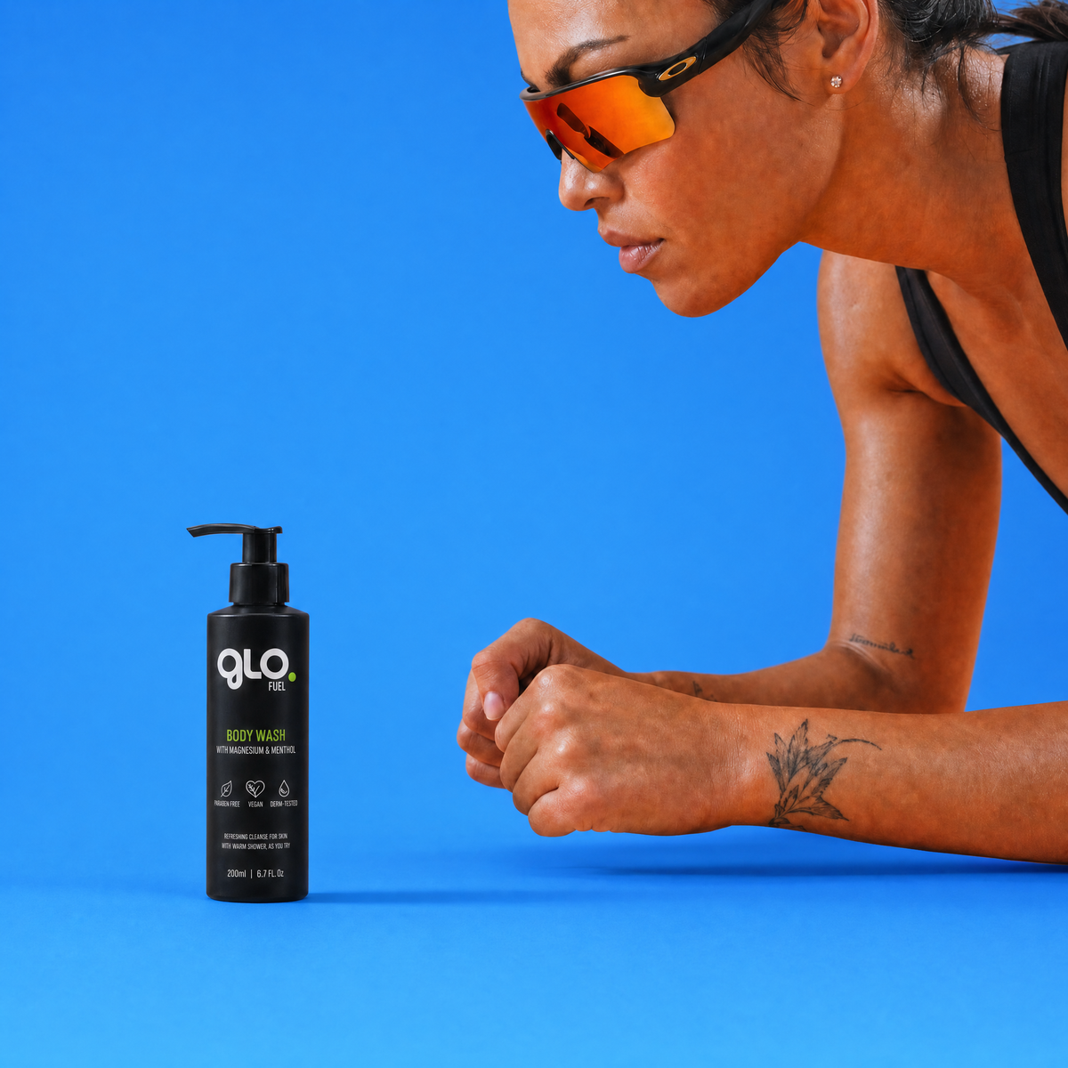 A bottle of GloFuel Body Wash is shown on a bright blue background next to a woman in athletic sunglasses and a black sports top, leaning forward.
