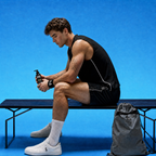 A man in a black athletic tank top and shorts sits on a bench against a bright blue background, holding a black pump bottle of GloFuel body wash. A gray drawstring bag rests beside him, and he wears white socks and white sneakers.